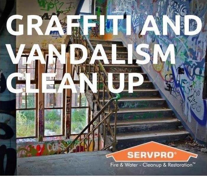 SERVPRO logo on a sign stating that SERVPRO does graffiti and vandalism cleanup. A building with graffiti is the background